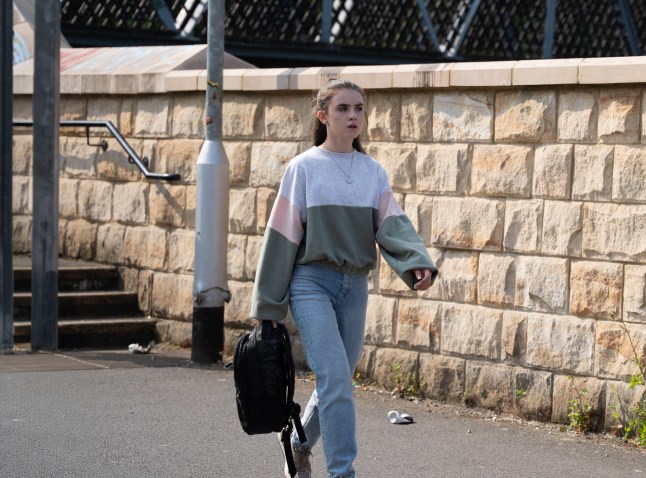 April walking through a street carrying a bag in Emmerdale