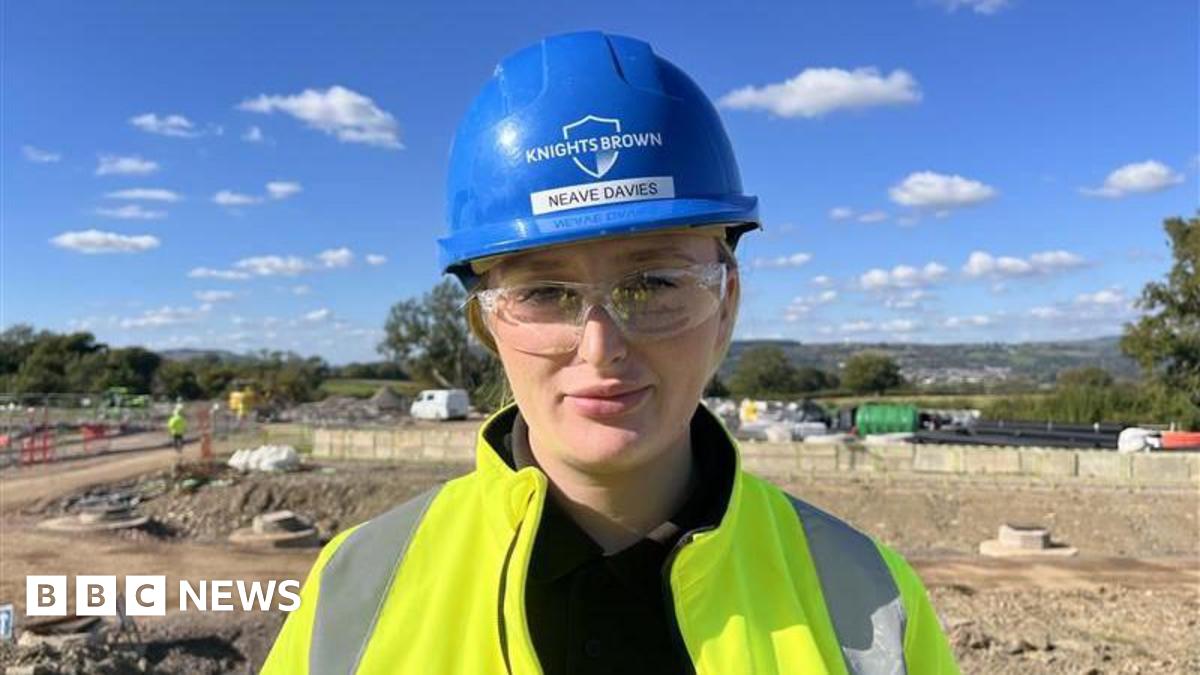 Jack Little on a construction site, wearing a high vis jacket, a blue hard hat, and protective glasses.