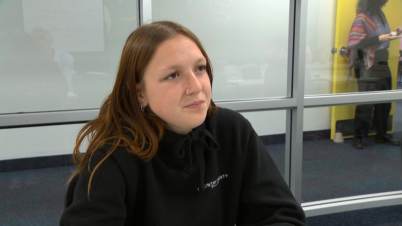 A young woman with long brown hair and a nose rings sits at a table.