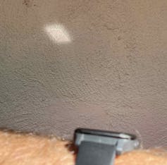 A watch on somebody's hairy wrist with a small oblong of light on a wall next to it.