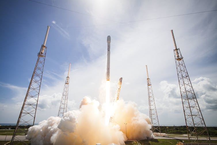 A tall, narrow rocket launching on a pillar of fire, above billowing clouds of steam.