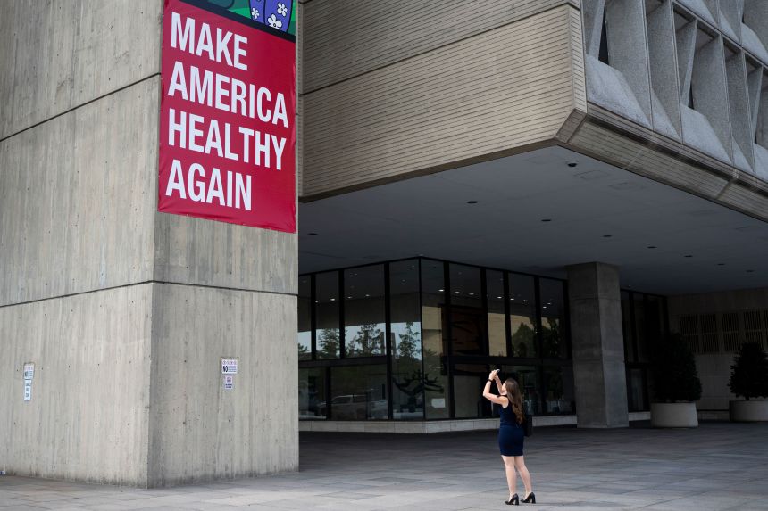 A woman takes a photo of the Make America Healthy Again sign hanging outside the Department of Health and Human Services in Washington, DC, in September.