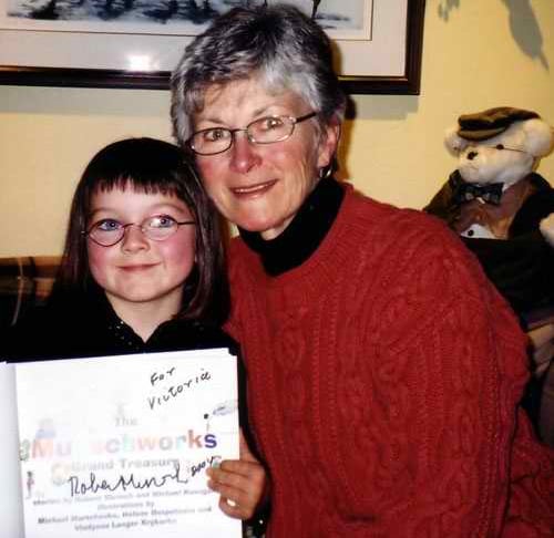 A young girl with a black bob with bangs, holding a signed book, alongside an older woman with short grey hair.