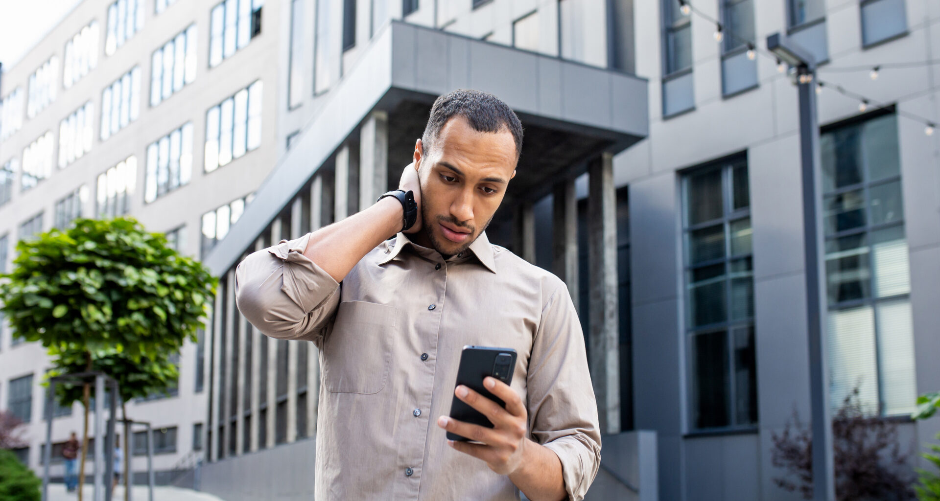 Disturbed arab man rubbing head with hand while looking at mobile phone screen on background of office building, investing myths, losing money