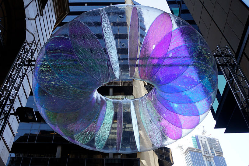 floating oculus installation shimmers in shifting chromatic light above brooklyn's streets