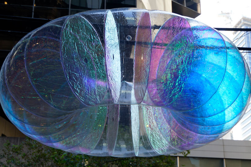 floating oculus installation shimmers in shifting chromatic light above brooklyn's streets