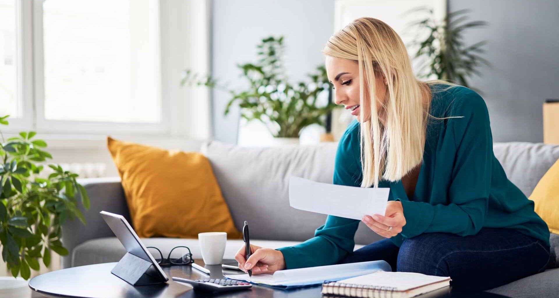 A woman sits on a couch and analyzes her bills.