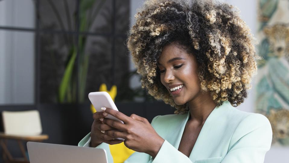 Smiling professional black woman with laptop using smart phone upskilling