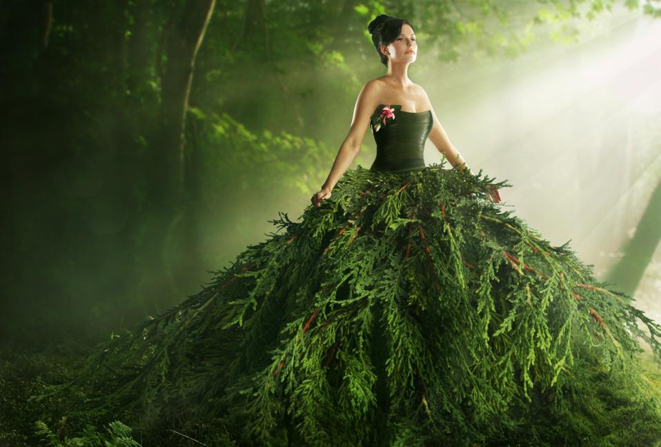 Model wearing a large green gown in the forest made from plants.