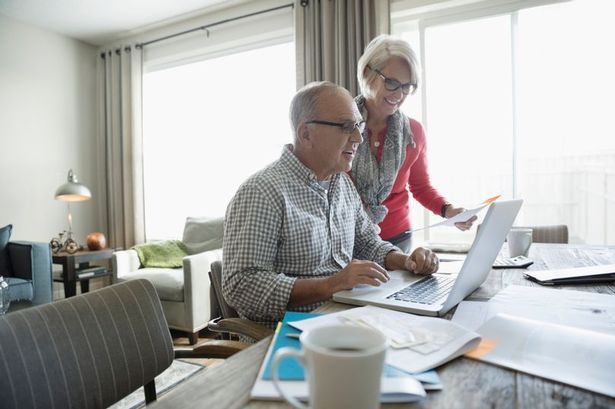 An elderly man and woman are working together on a computer 