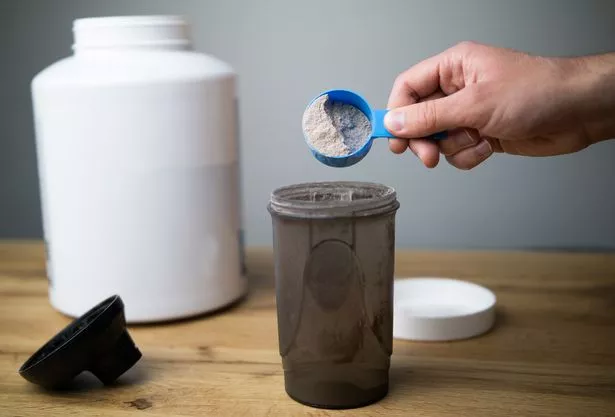 Close up of a man preparing protein shake. Pouring chocolate protein powder in a shaker