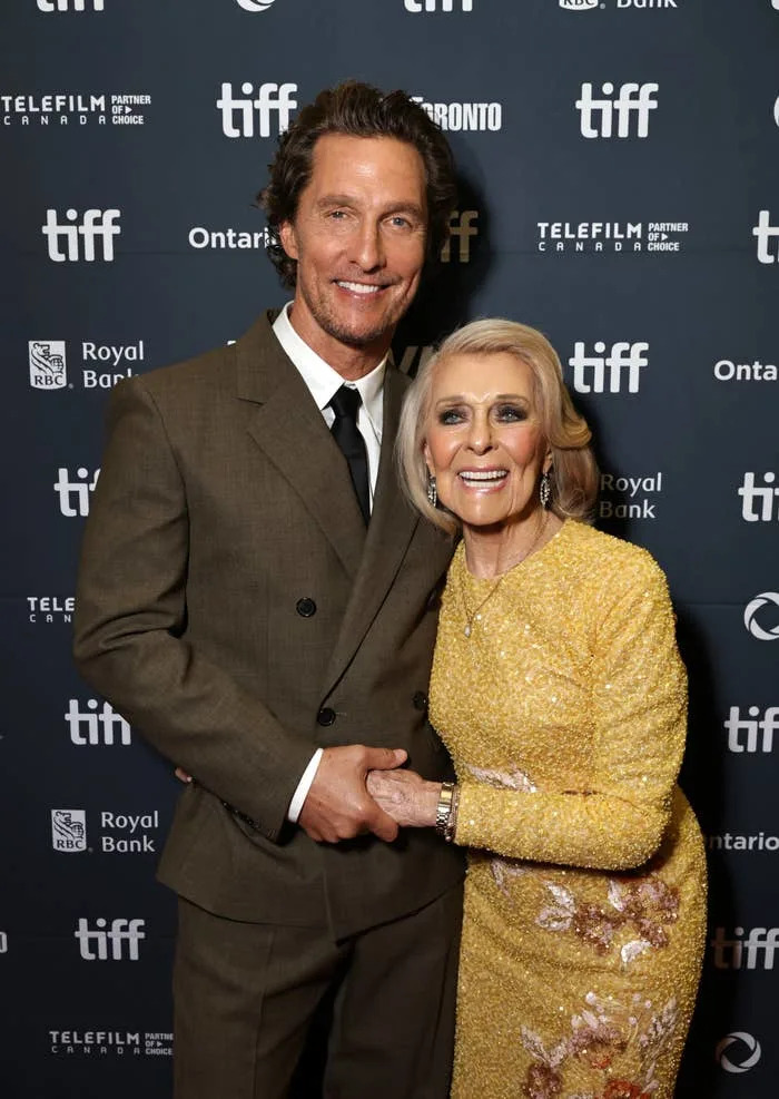 Two people smiling on a red carpet, dressed in a brown suit and a sequined dress, attending the Toronto International Film Festival (TIFF)