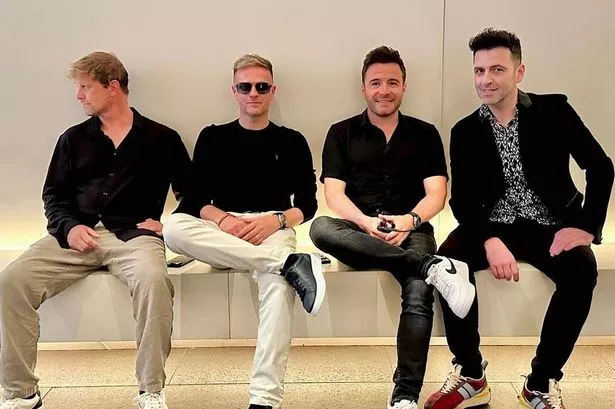 Westlife is pictured smiling together on a bench