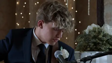 Fulwell Productions A screenshot of the Gavin and Stacey finale of Oscar Hartland, who plays Neil the baby, is wearing a suit and is singing into a microphone. 