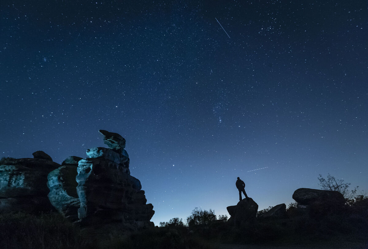 A plane and a satellite pass by as a man stargazes at Brimham Rocks in Yorkshire as the Orionid meteor shower reaches its peak