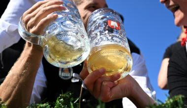 Revellers wearing traditional Bavarian costumes cheer with their beer mugs during the costume parade