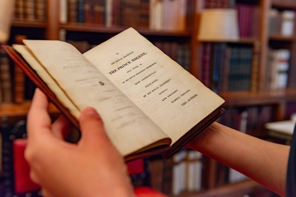 Open book held by a person in a library setting.