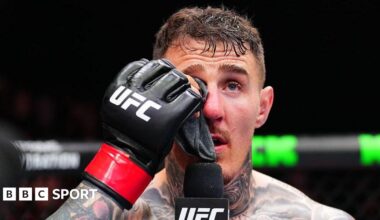 Tom Aspinall holds a cloth to his eye and speaks into a microphone