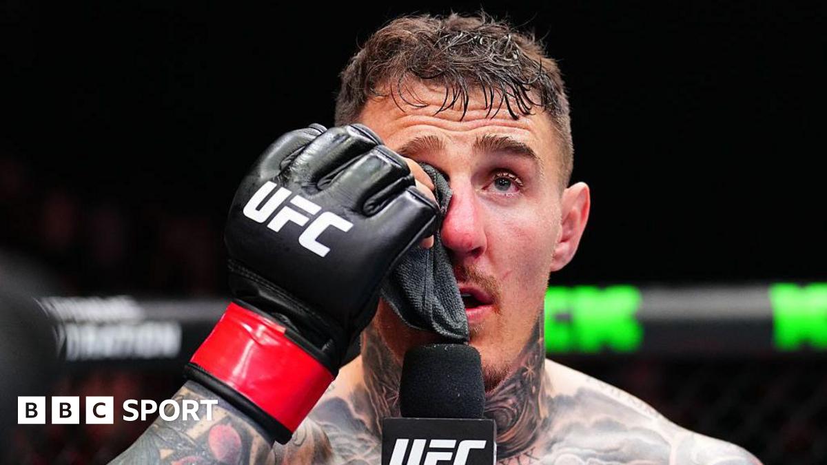 Tom Aspinall holds a cloth to his eye and speaks into a microphone