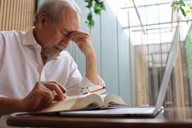 Feeling sick and tired. Frustrated elderly man massaging his nose and keeping eyes closed while sitting at his working place in office