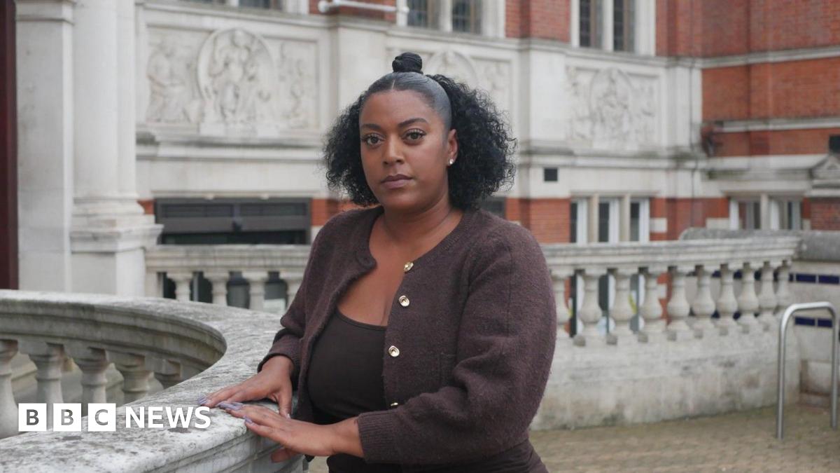 Nadine is standing outside, looking at the camera. She has black curly hair and is wearing a brown cardigan.