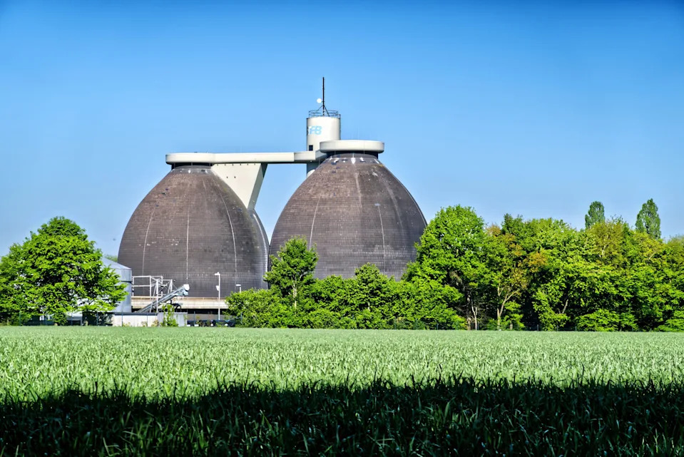 Two large anaerobic digesters dominate the landscape, converting organic waste into biogas, a sustainable energy source, surrounded by lush greenery a