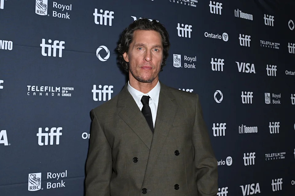 Man in a formal double-breasted suit poses on the TIFF red carpet with sponsor logos in the background