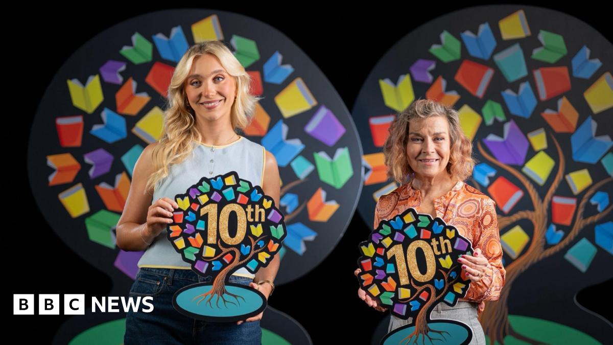 Ali and Cecilia are both holding Book Week symbols, which are in the shape of a tree with multi-coloured leaves and the word 10th in the centre. Ali has long blonde hair and is wearing a blue sleeveless top. Cecelia has shoulder length hair and is wearing an an orange patterned blouse.
