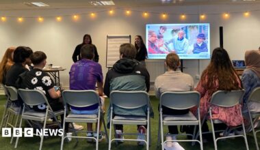 A group of young people sitting in a semi-circle chairs, listening to a presentation.