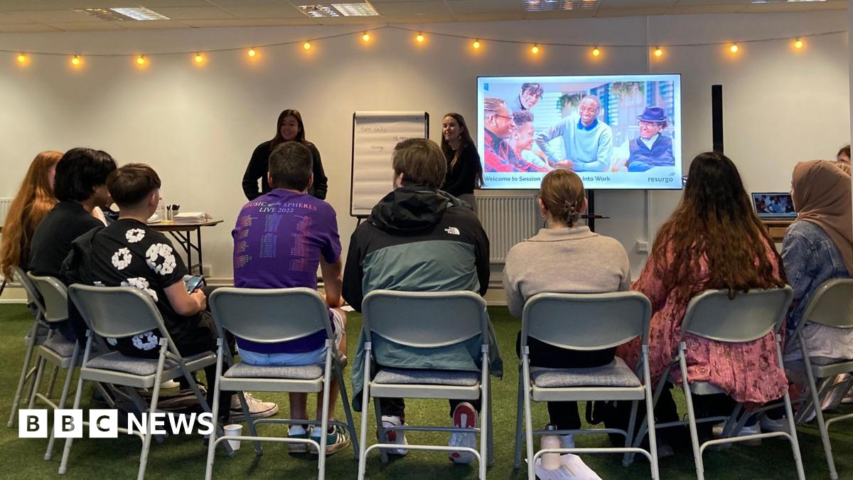 A group of young people sitting in a semi-circle chairs, listening to a presentation.