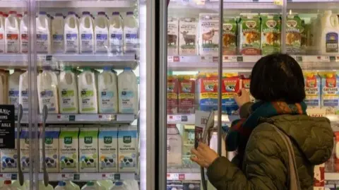 Getty Images A woman reaches into a supermarket fridge to select a carton of milk. 