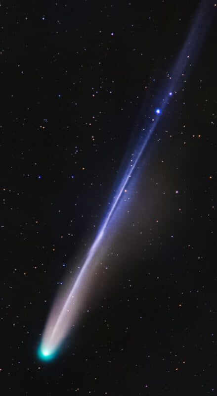 A bright green comet with a glowing white core and a long, blue-tinged tail streams across a star-filled night sky.