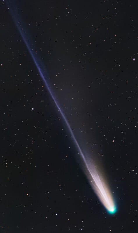 A bright comet with a glowing greenish core and a long, luminous blue and white tail streaks across a star-filled night sky.