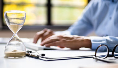 person typing on keyboard with glasses and hourglass next to it