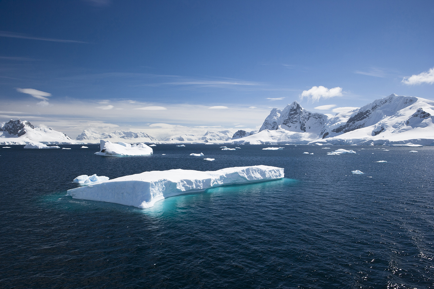 A glacier floating in the sea below a blue sky.