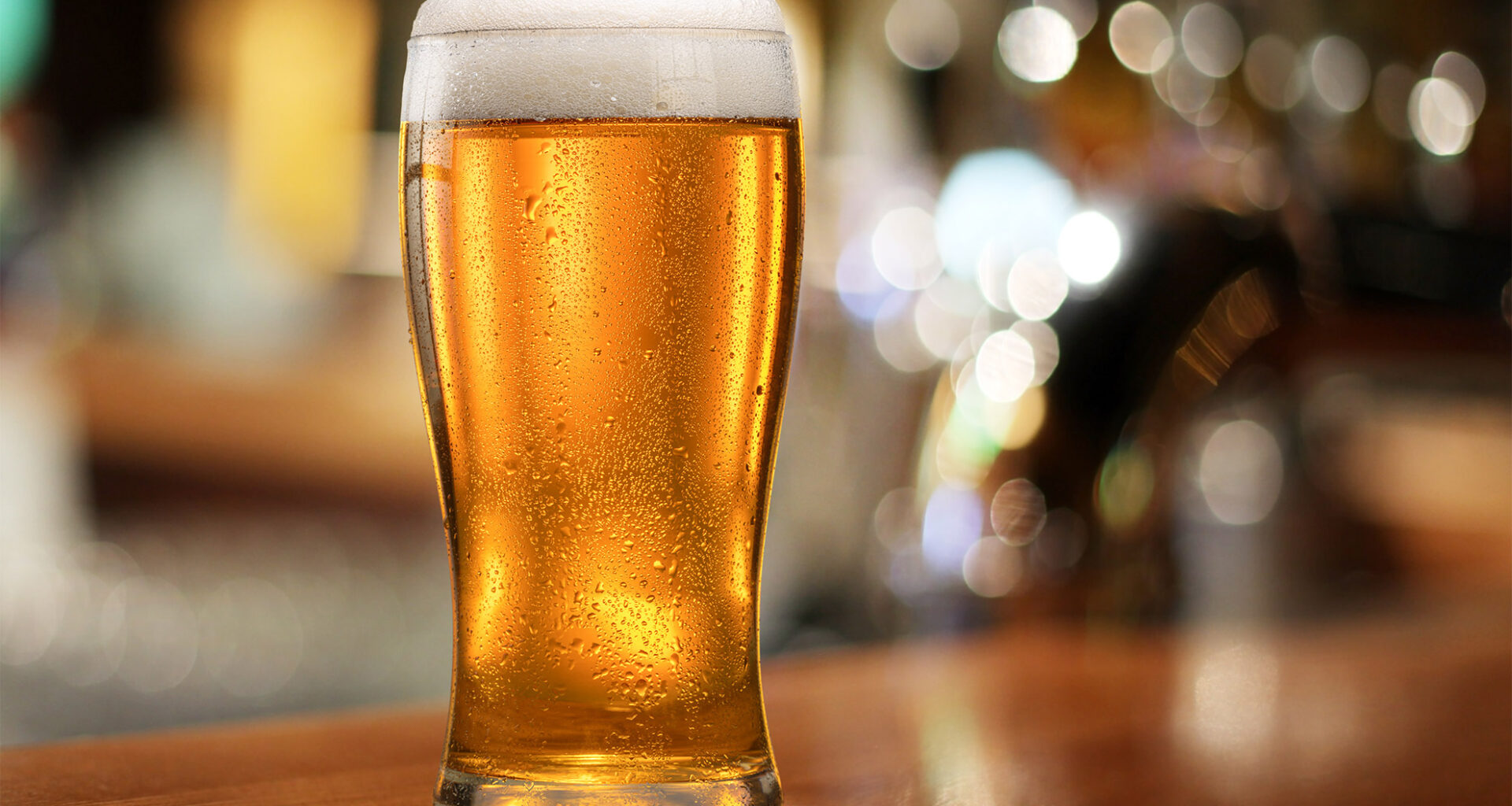 Glass of chilled beer on wooden bar table.