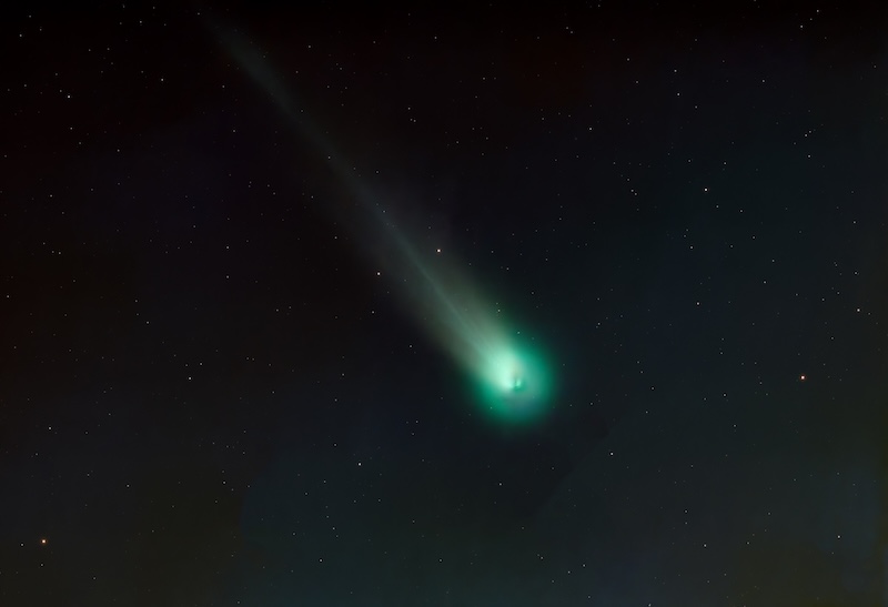 Several small glowing bits inside a fuzzy green head of a comet with a greenish tail.