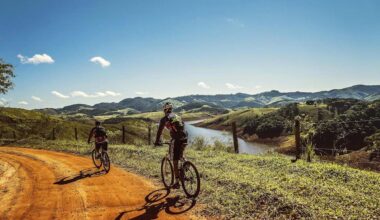 Two cyclists exercise in nature along a scenic trail with a river and greenery in the background.
