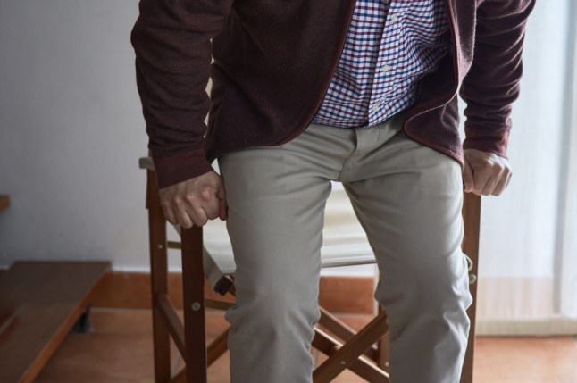 A mature man has difficulty getting up from an armchair in the living room of his home.