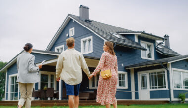 Real Estate Agent Showing a Beautiful Big House to a Young Successful Couple. People Standing Outside on a Warm Day on a Lawn, Talking with Businesswoman, Discussing Buying a New Home.
