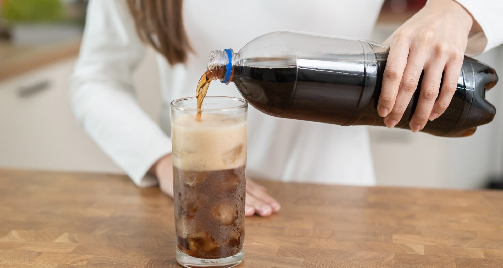 woman pouring fizzy cola soda into a glass of ice