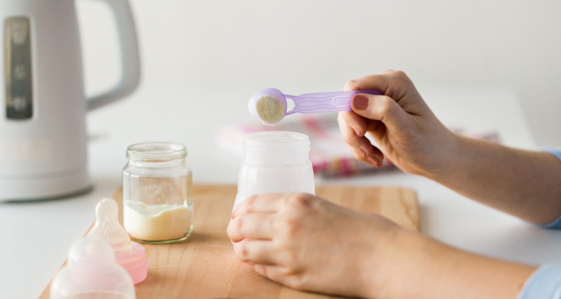 Mother hands with baby bottle and scoop preparing infant formula milk