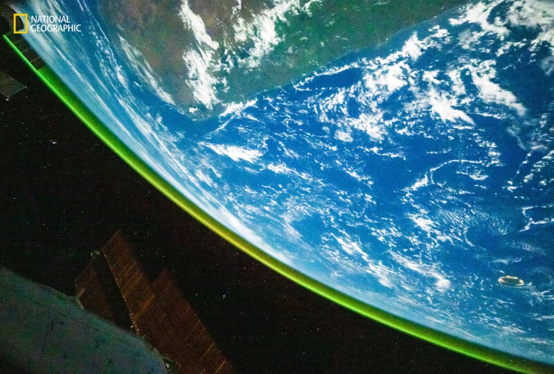 A view of Earth from space shows the planet’s blue oceans, white clouds, and part of a continent, with a thin green line of atmosphere visible along the edge. The National Geographic logo appears in the top left corner.