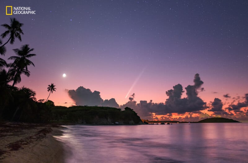 A serene tropical beach at dusk with silhouetted palm trees, calm water, and a colorful sky showing stars, a crescent moon, and a bright comet above the horizon. The National Geographic logo appears in the top left corner.
