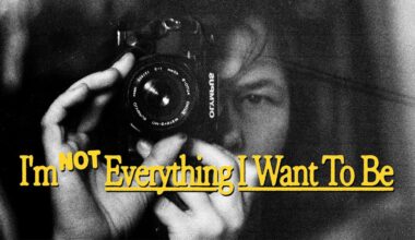 A person holds a camera close to their face, partially obscured in black and white. Yellow text over the image reads, "I'm NOT Everything I Want To Be.