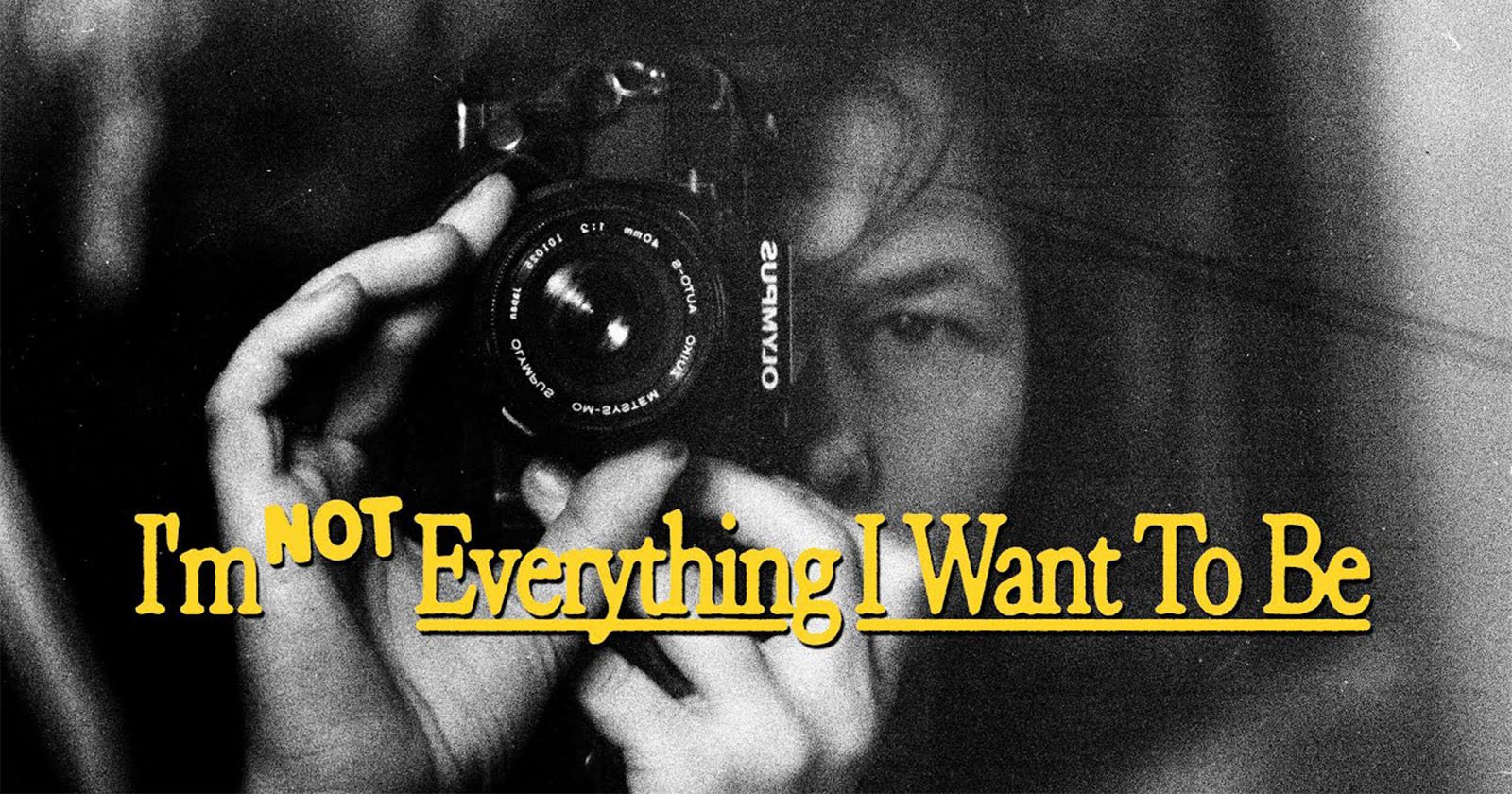 A person holds a camera close to their face, partially obscured in black and white. Yellow text over the image reads, "I'm NOT Everything I Want To Be.