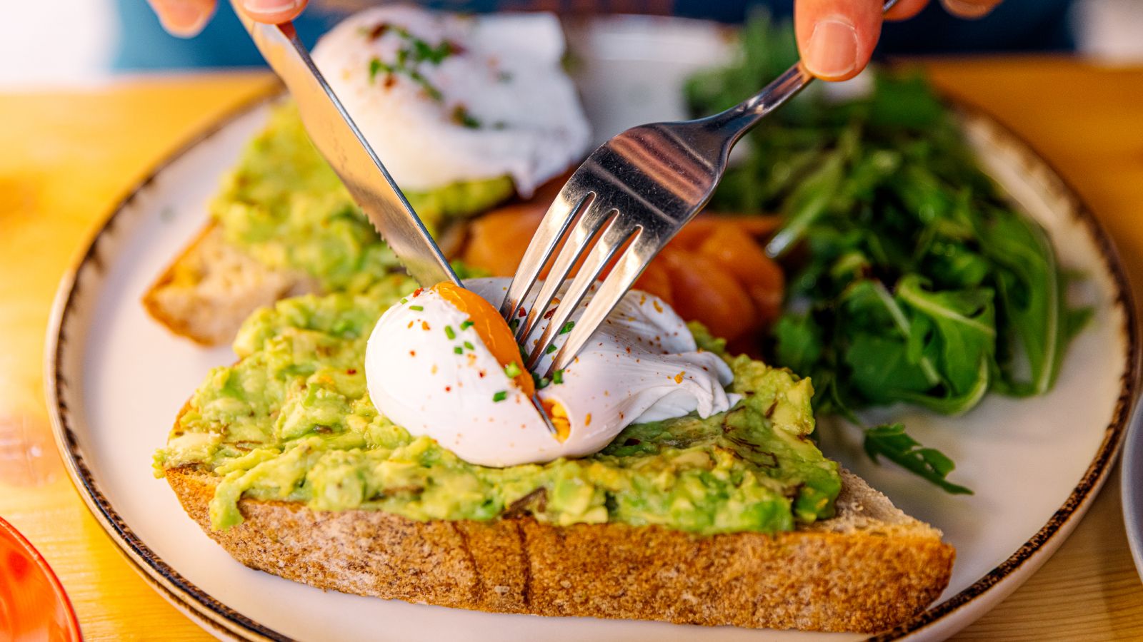 Person eating avocado toast with poached egg and salmon, close-up view