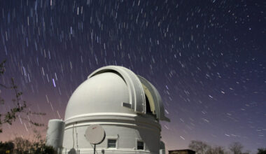 Big, white telescope dome with deep blue sky above it with many stars, appearing as short streaks.