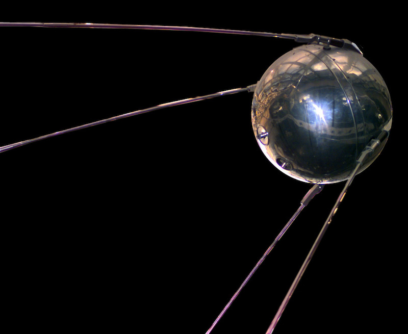 Shiny metallic ball with four long thin antennas, in space.