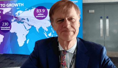 Stephen Timms head and shoulders in a suit and tie, smiling, with a map of the world in the background